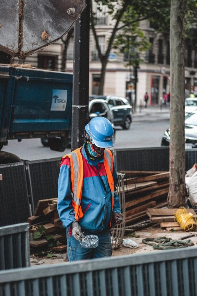 Side view of male worker in protective helmet and uniform standing on construction site in big contemporary megapolis